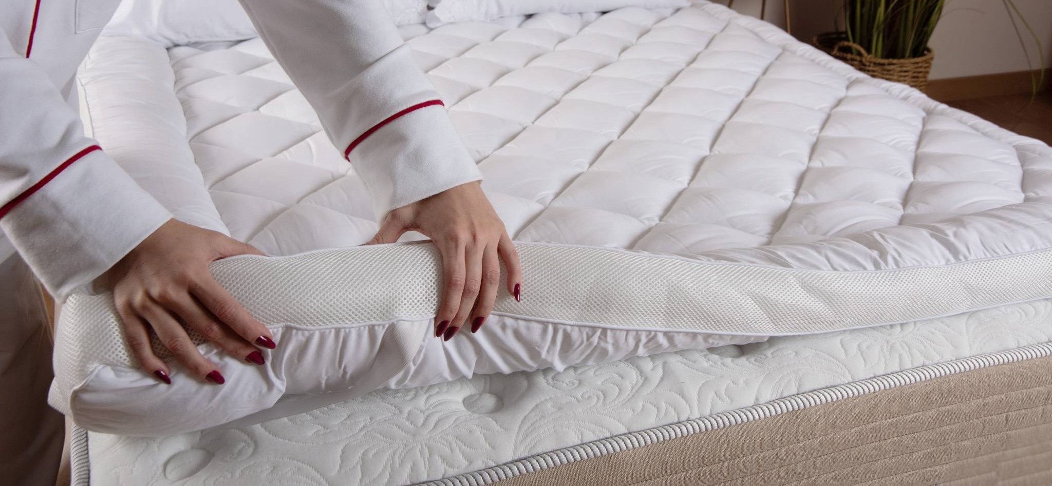 mulher de pijama mostrando um pillow top sobre a cama. ela aperta as laterais mostrando a maciez