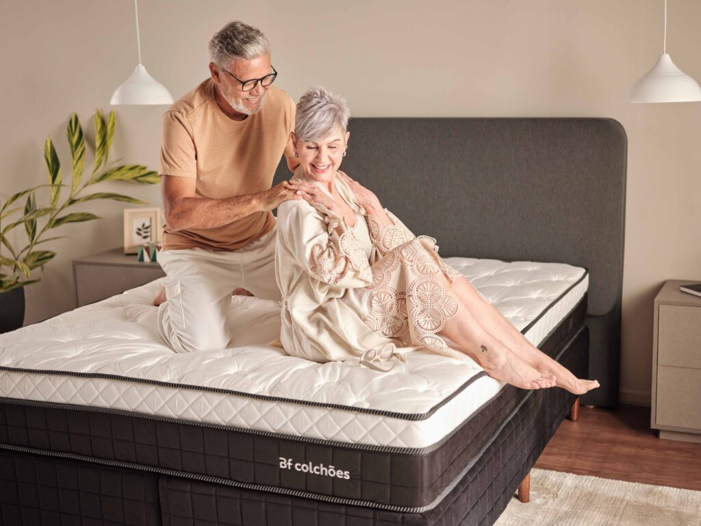 casal de idosos feliz sentado em um colchão para dores nas costas. o homem faz massagem nas dores nas costas da mulher